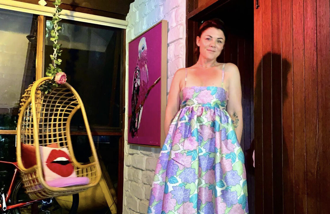 © Em Rusciano / Instagram. Em Rusciano wearing a pastel dress, next to a hanging chair with cushion.