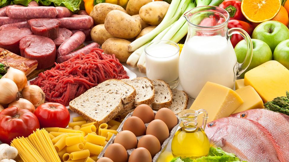 A table covered in a range of food including eggs, milk, meats, fruits, and vegetables