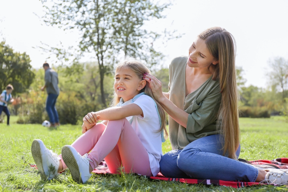 A mother and daughter sitting on grass together. The mother is touching the daughter’s hair.