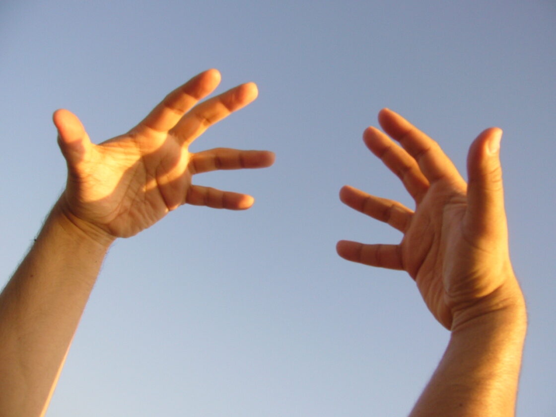 Two hands in the air, against a pale blue sky.