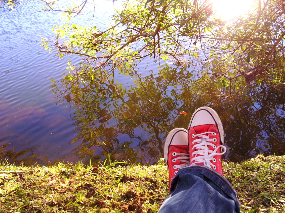 A pair of feet in trainers, evidently lying down on grass with a view of trees and sunshine.