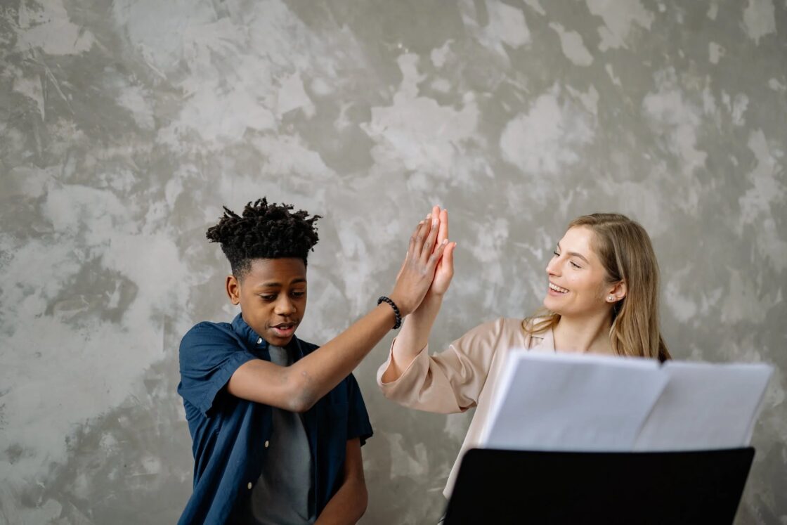 A child and adult high fiving. The adult is smiling.