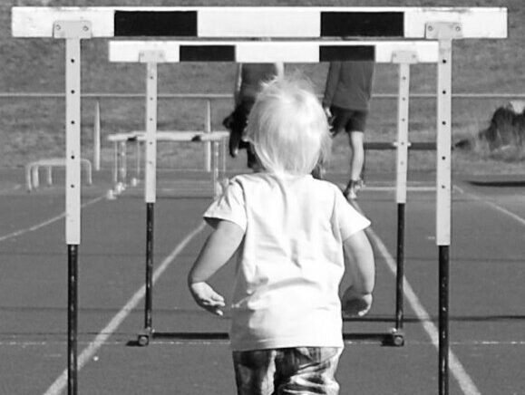 Black and white photo of a small child running towards hurdles