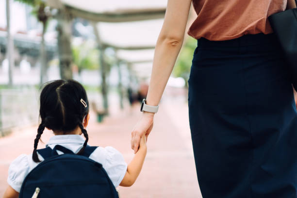 A mother holding the hand of a small child in school uniform