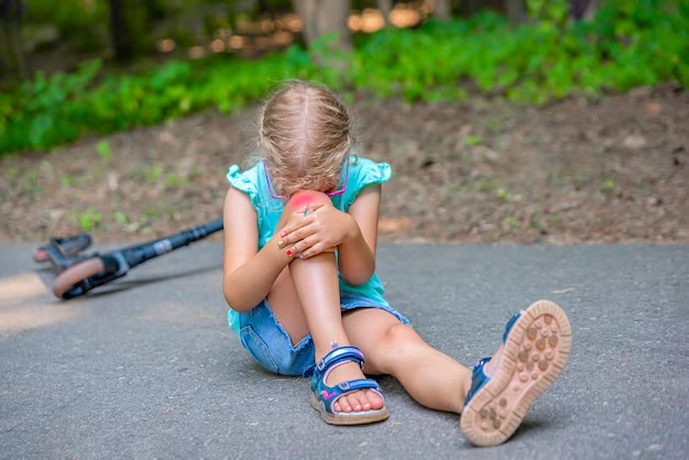 A girl clutching her knee and looking sad, with a scooter behind her