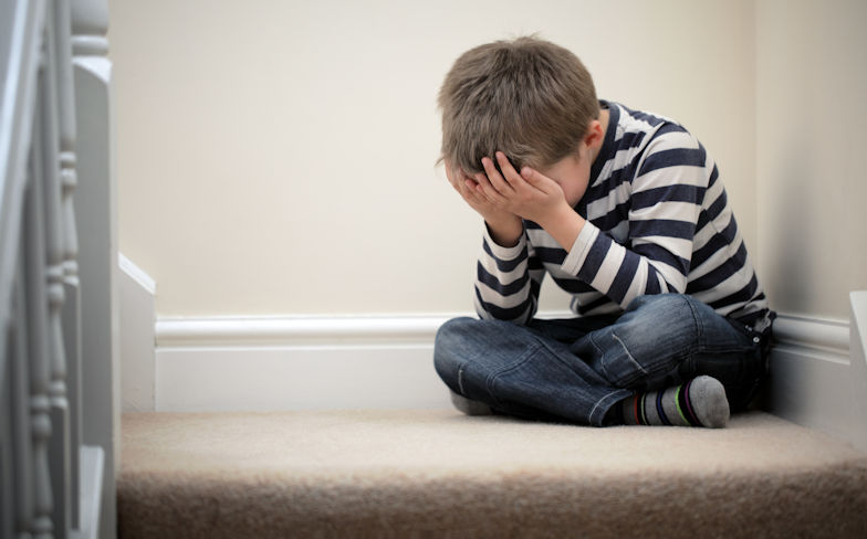 An upset child sitting on stairs with their head in their hands