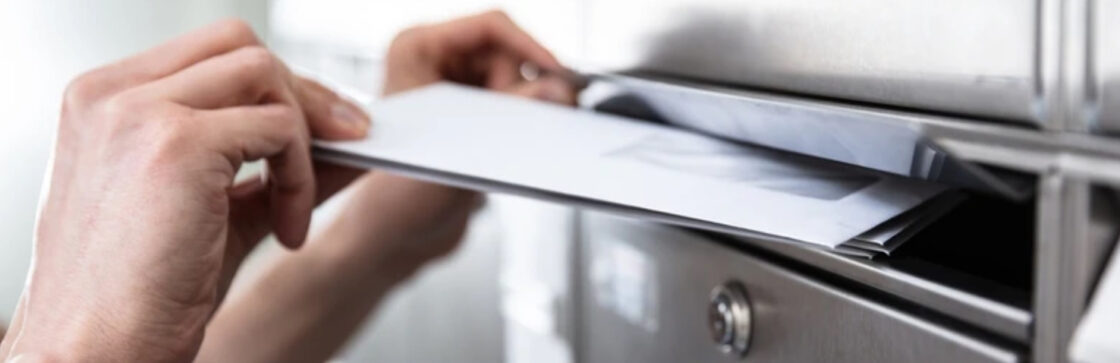 A hand placing a letter in a mailbox