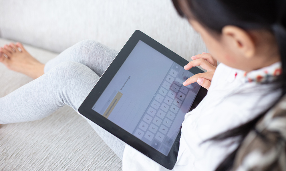 A child typing on a tablet which may be an AAC device.